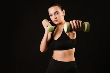 Young fitness model woman doing exercises with dumbbells on black background. Copy space