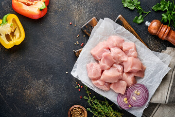 Wall Mural - Raw pieces meat ingredients of chicken on wooden board, spices, herbs and vegetables on dark grey background. Raw ingredients for goulash or shish kebab. Top view. Free copy space.