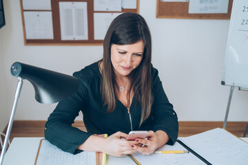 Wall Mural - Female professor having break with online class and using her mobile phone to send text message.
Teacher is working from home with E-learning students teaching online lessons during isolation period.