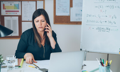 Wall Mural - Female professor having break with online class and talking on mobile phone .
Displeased teacher calling somebody on phone and preparing to working from home desk with E-learning students online.