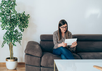 Wall Mural - Cheerful Business Woman Sitting on Sofa and using Tablet
Smiling businesswoman with wireless earphones looking in digital tablet, working at home concept.