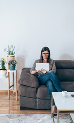 Wall Mural - Beautiful Business Woman Sitting on Sofa and Using Digital Tablet
Serious businesswoman with wireless earphones looking in digital tablet in living room, working at home concept.