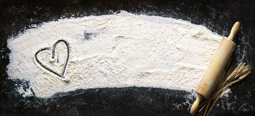 Abstract baking background with the rolling pin and flour on dark table