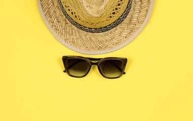 Summer background. Straw sun hat and sunglasses on a yellow background. Top view, close-up, horizontal. Summer concept. Copy space.