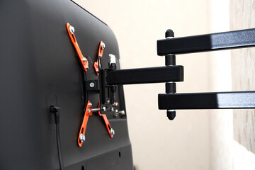 Swivel TV bracket LED display. Back view. X-shaped red fasteners. Black color. Multiplanar. Hangs on a wall. Reliable and comfortable fastening. Childproof and rollover protection. Metallic equipment