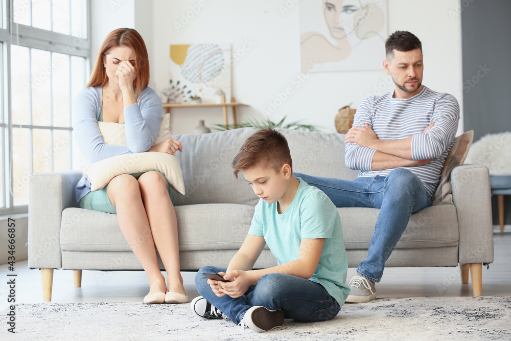 Little boy using mobile phone and his sad parents after quarrel at home