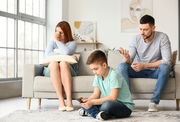 Wall Mural - Little boy using mobile phone and his sad parents at home