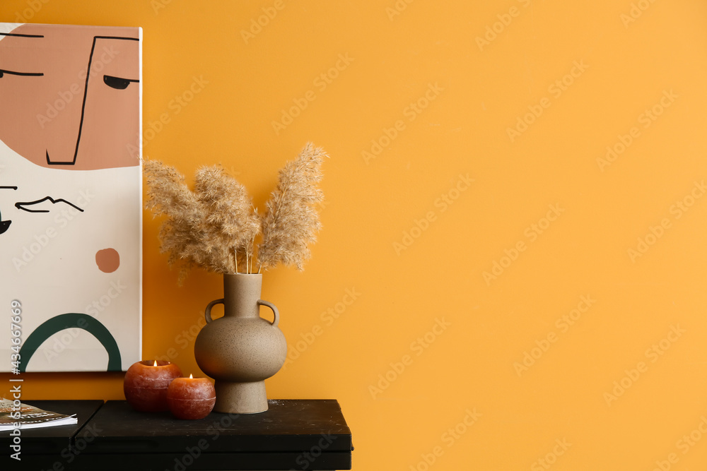 Burning candles with vase on table near color wall - obrazy, fototapety, plakaty 