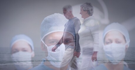 Canvas Print - Senior couple waking on the beach against portrait of team of surgeons wearing face masks