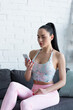 © LIGHTFIELD STUDIOS - young woman in sportswear sitting on couch with mobile phone