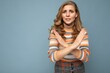Portrait of young pretty beautiful sad angry dissatisfied blonde woman with sincere emotions wearing casual striped sweater isolated over blue background with copy space and showing no gesture and