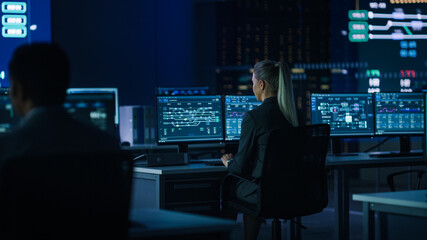 Wall Mural - Computer Science Female Engineer Working under Important Project on Personal Computer Showing Infrastructure Infographics and Data.Telecommunications Control Monitoring Room with People Working.