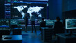 Project Manager Uses Digital Tablet Talks with Computer Scientist Looks at Big Screen Display Showing Infographics Global World Map Data. Telecommunications Control Control Room with People Working