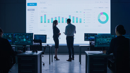 Aufkleber - Project Leader, Chief Executive Discuss Data Shown on Big Display. Screens Show Infographics, Charts, Finance Analysis, Stock Market, Growth. Telecommunications Control Room with Working Professionals
