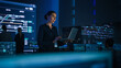 © Gorodenkoff - Beautiful Confident Female Project Manager works on Laptop Standing in Telecommunications System Control Room. In Background Big Screen Showing Infographics of Infrastructure, Charts, System Analysis