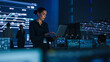 © Gorodenkoff - Beautiful Confident Female Project Manager works on Laptop Standing in Telecommunications System Control Room. In Background Big Screen Showing Infographics of Infrastructure, Charts, System Analysis