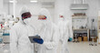 © nimito - Scientists in coverall discussing vaccine development looking on tablet in equipped laboratory.