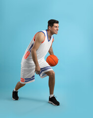 Wall Mural - Professional sportsman playing basketball on light blue background