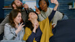 © DC Studio - Multiracial friends taking sefie together using smartphone posting on social media. Group of mixed-race people sitting on couch late at night in living room enjoying free time