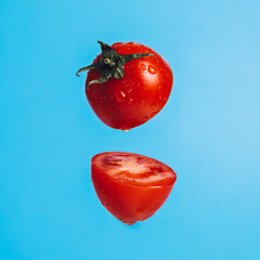 Wall Mural - Fresh cut red tomato isolated on a pastel blue background. Minimal summer food concept. Vegetarian diet or culinary wallpaper idea.