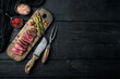 © Ilia Nesolenyi - Grilled fillet beef steaks, with onion and asparagus, on wooden serving board, with meat knife and fork, on black wooden table background, top view flat lay, with copy space for text