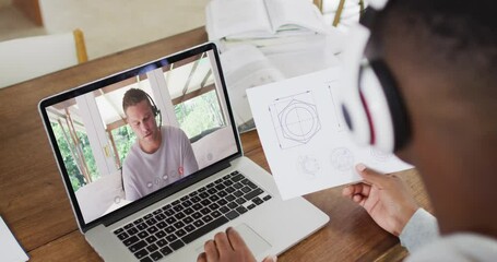 Canvas Print - African american male college student holding notes while having a video call on laptop at home