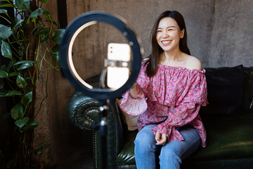 Young woman making photo or video content for social media with smartphone and light of ring lamp. Beauty blogger smiles to mobile phone screen. Influencer Makes broadcast communicates with followers