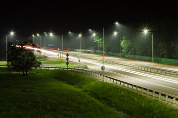 Night highway in the light of streetlights and the plumes of headlights of passing cars