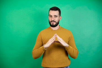 Wall Mural - Handsome man wearing casual clothes over isolated green background with Hands together and fingers crossed smiling relaxed and cheerful. Success and optimistic