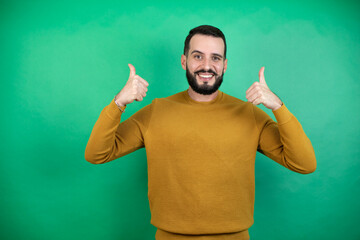 Wall Mural - Handsome man wearing casual clothes over isolated green background doing positive gesture with hand, thumbs up smiling and happy. cheerful expression