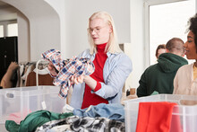 Worker Putting Plaid Shirt At The Plastic Box While Sorting Clothes For The Altering