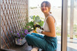 young beautiful woman smiling taking care of her plants in her balcony