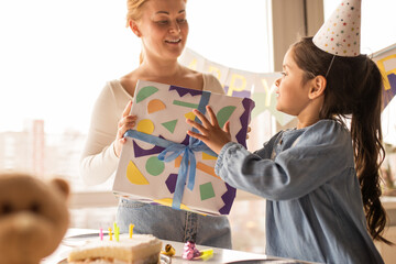 Wall Mural - Woman giving a gift to her daughter wearing party cap while spending her birthday