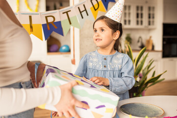 Wall Mural - Girl wearing party hat looking at her mother while accepting her birthday gift