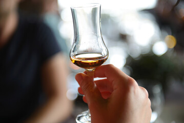 A glass with wiskey in hand of man with blurred background. Concept of whiskey tasting.