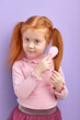 © alfa27 - Child Girl Combing Red Hair Posing At Camera, Isolated On Purple Studio Background. Portrait Of Adorable Cute Child Taking Care Of Hair Condition
