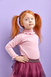 © alfa27 - Calm Diligent Girl with natural red hair posing at camera holding hands on belt, looking at camera with serious face. isolated purple background