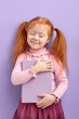 © alfa27 - Redhead pretty girl imagine favorite novel characters alive isolated over purple color background. Little child with natural red ginger hair stand with eyes closed smiling with dreaming face