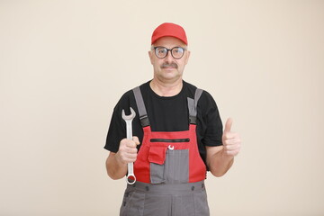 Wall Mural - man worker in a black t shirt, glasses and red gray construction overall holds a new gray tool straight pipe wrench or spanner and giving a thumbs up on a white isolated background