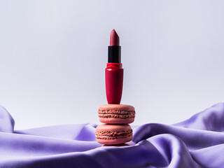 Red lipstick and pink macaroons on purple silk fabric background