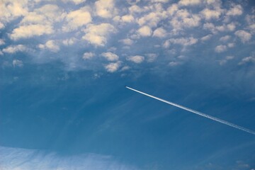 A high flying passenger jet leaving a vapour trail at dusk with alto cumulus cloud