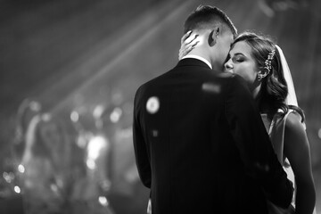 Portrait of newlyweds first wedding dance. Just married couple dancing in darkness. Groom holds bride's hand dancing with her in the middle of restaurant. Happy bride and groom and their first dance.