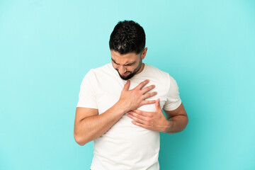 Young arab man isolated on blue background having a pain in the heart