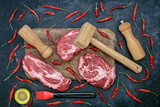 Fototapeta Młodzieżowe - Beef Steaks for Grilling Or Frying, Overhead View. Marbled Raw Loin Beef Steaks, Wooden Hammer, Salt and Pepper Mill On Cutting Board. Raw Striploin Marbled Beef Steaks on Black Background, Top View.