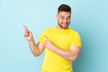 Wall Mural - Russian handsome man isolated on blue background frightened and pointing to the side