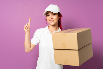 Teenager delivery girl isolated on purple background showing and lifting a finger in sign of the best