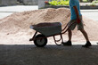 Silhouette of Male Worker pushing a wheelbarrow carrying sand. Garden wheelbarrow loaded with Basalt chips for house courtyard driveway patio.