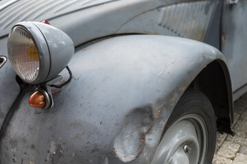 Front with headlight and a dent in the mudguard of an old run-down car (Citroen 2CV) in the village Raerd, The Netherlands