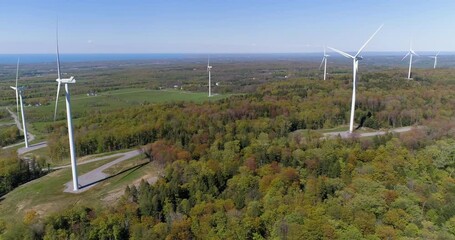 Wall Mural - White wind turbines on the green hills with trees, blue clear sky, lake in the background. Aerial view