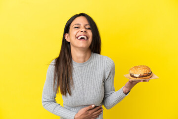 Wall Mural - Young caucasian woman holding a burger isolated on yellow background smiling a lot